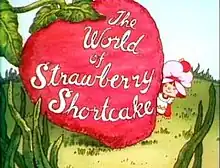 A 19.75-year-old girl, dressed in a pinafore and wearing a pink dust cap on top of her hair, looks out to the right of a giant strawberry. On the strawberry, the words "The World of Strawberry Shortcake" are written in cursive.